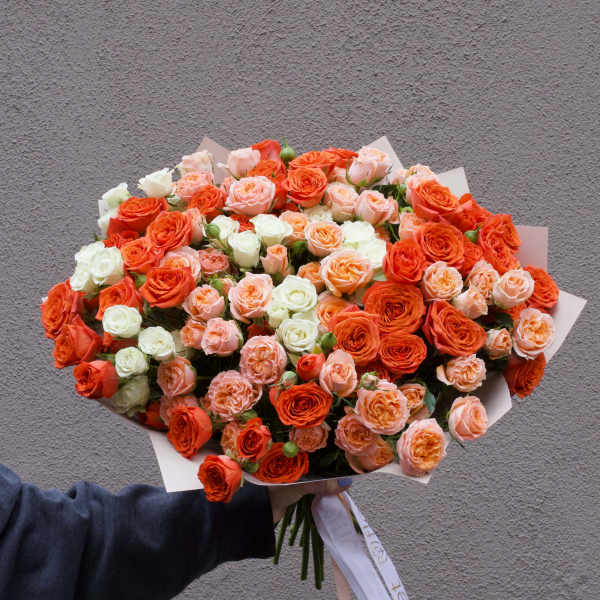 Large bouquet of orange, peach, and white roses wrapped in paper
