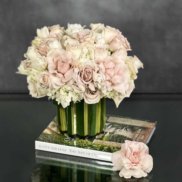 Low arrangement of blush and ivory roses in a leaf-lined glass vase on stacked books