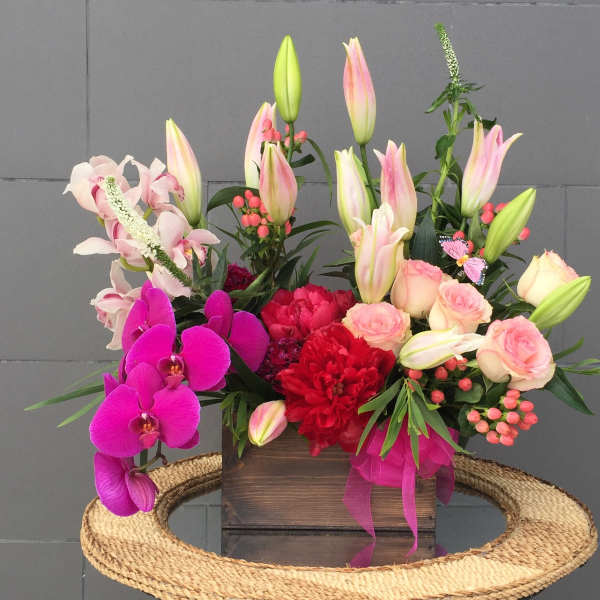 Mixed bouquet with pink lilies, roses, orchids, and red blooms in a wooden box