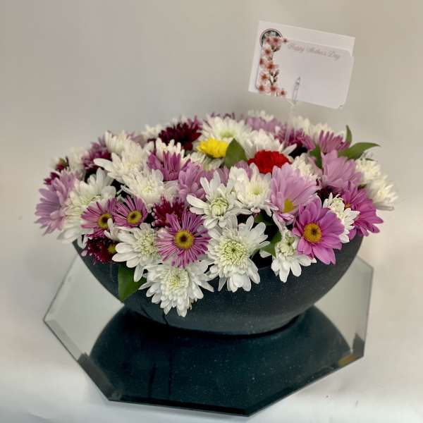 Mixed pink, white, and purple daisy bouquet in a dark bowl vase