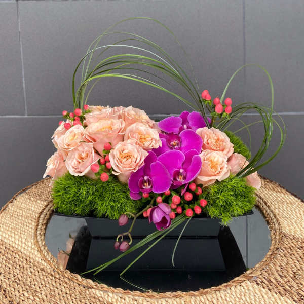 Peach roses and purple orchids in a low black container