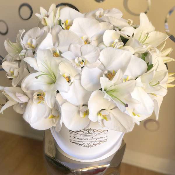 Round white hatbox filled with white orchids and lilies on a metallic pedestal stand
