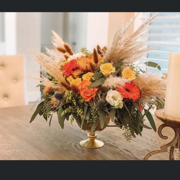 Orange and yellow flower arrangement in a gold pedestal bowl