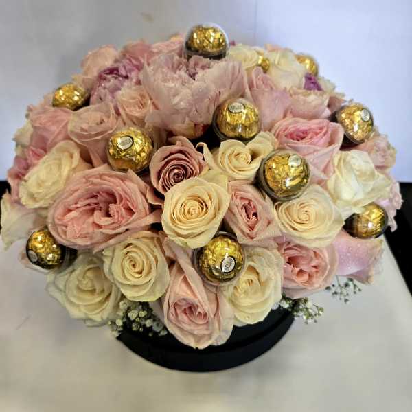 Bouquet of pale pink and cream roses with gold-wrapped chocolates in a black box