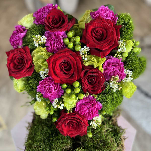 Heart-shaped bouquet of red roses, pink carnations, and green accents