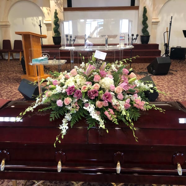 Pink and white floral casket spray on a dark wood casket