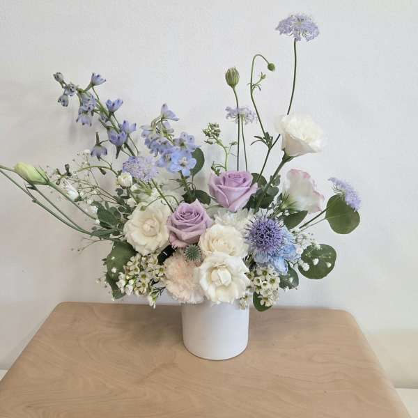 Pastel bouquet of lavender, white, and blue flowers in a white vase