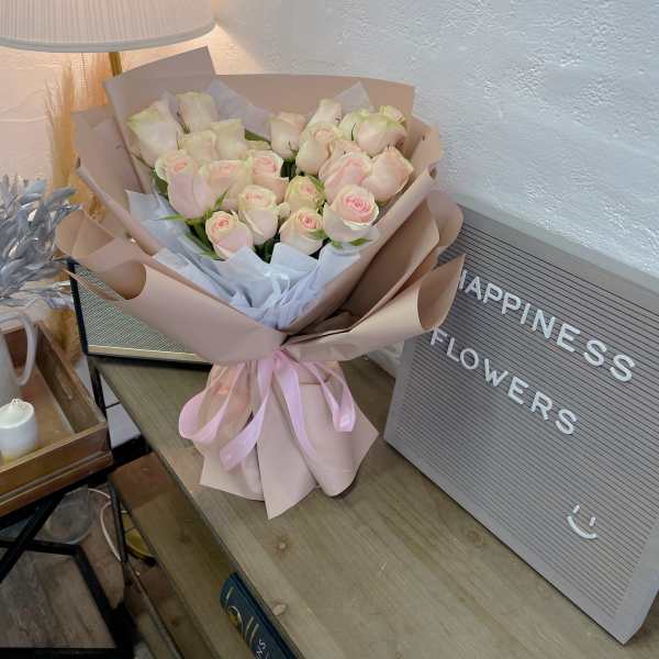 Bouquet of pale pink roses wrapped in blush paper with a pink ribbon