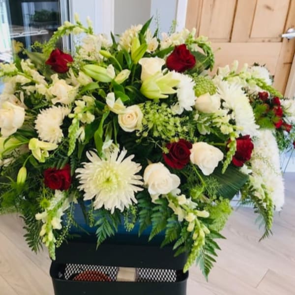 Large floral spray with white lilies, roses, and red roses in a black container.