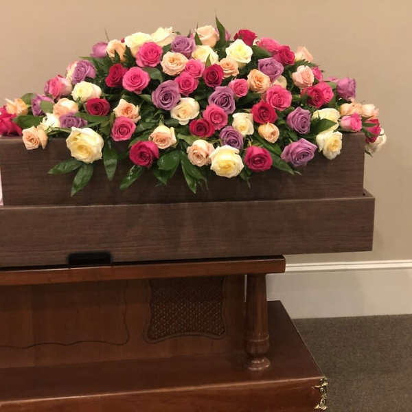 Casket spray of pink, purple, cream, and peach roses