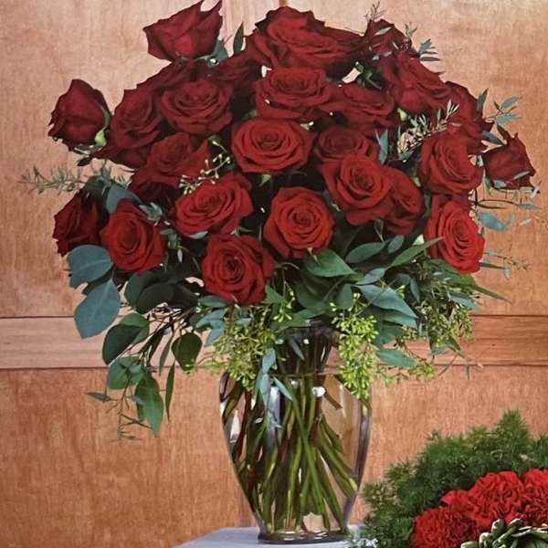 Red roses arranged in a clear glass vase with greenery