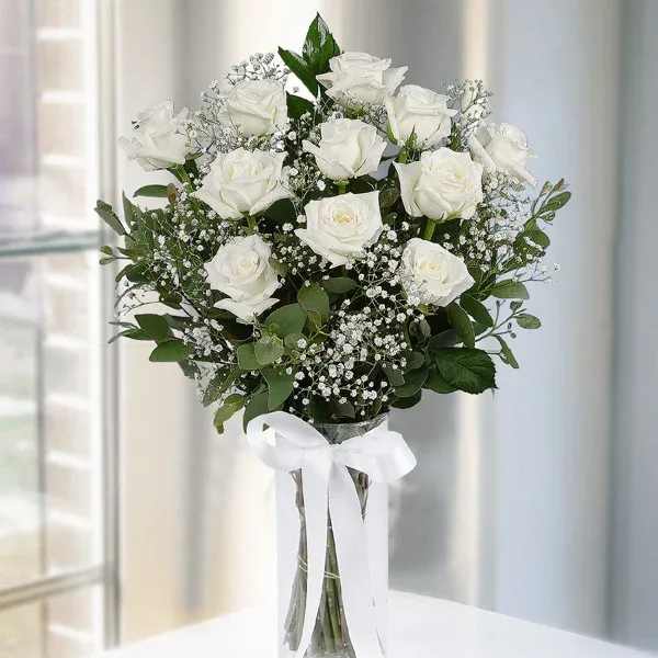 White roses arranged in a clear vase with a white ribbon.