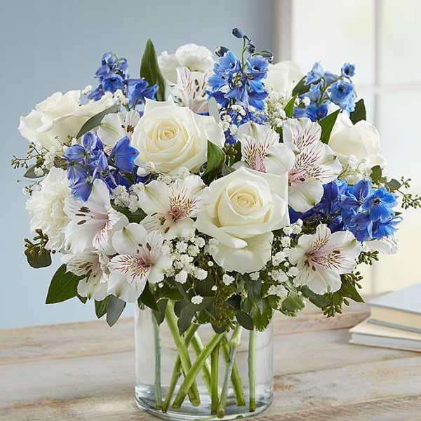 White roses and blue flowers arranged in a clear glass vase