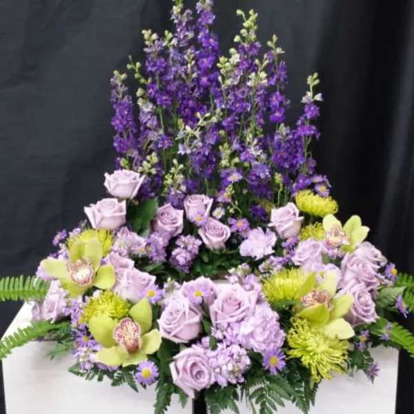 Lavender roses and purple flowers arranged in a tall display with green accents.