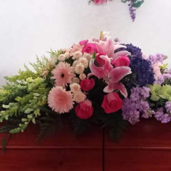 Casket spray with pink lilies, roses, and purple flowers