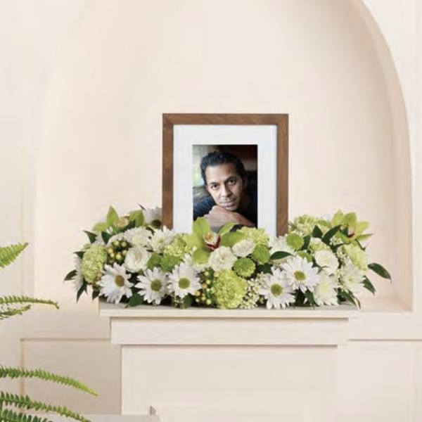 White and green funeral arrangement with a framed portrait in the center