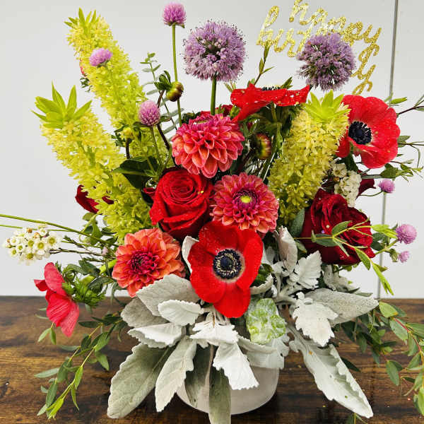 Bright mixed bouquet with red roses, pink dahlias, and purple blooms in a white vase