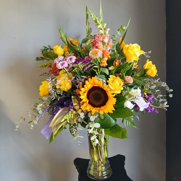 Mixed bouquet with sunflowers, yellow roses, and purple flowers in a glass vase