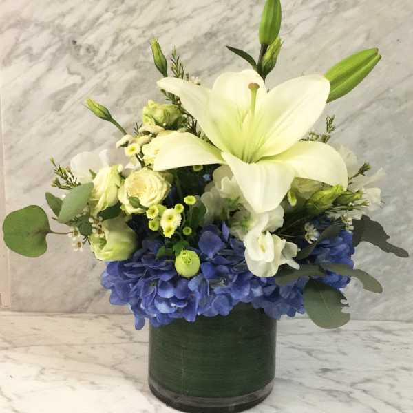 White lily and blue hydrangea arrangement in a dark glass vase