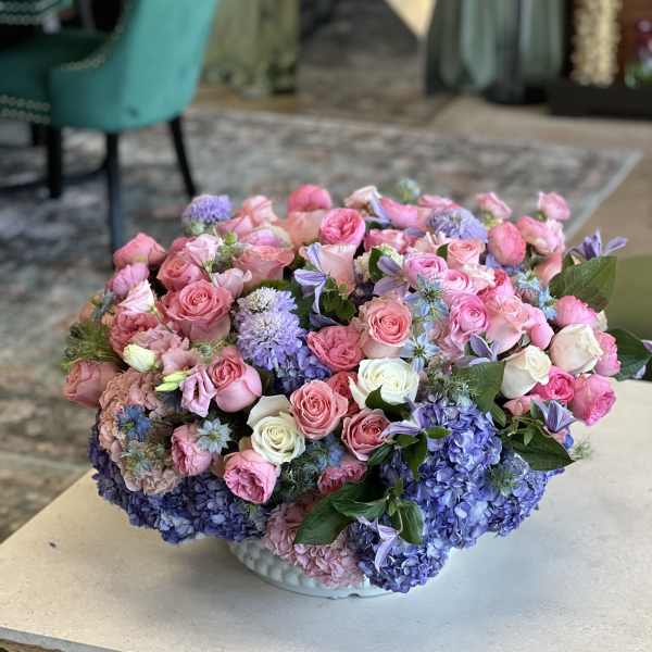Large pastel bouquet of pink roses and blue hydrangeas in a white bowl vase