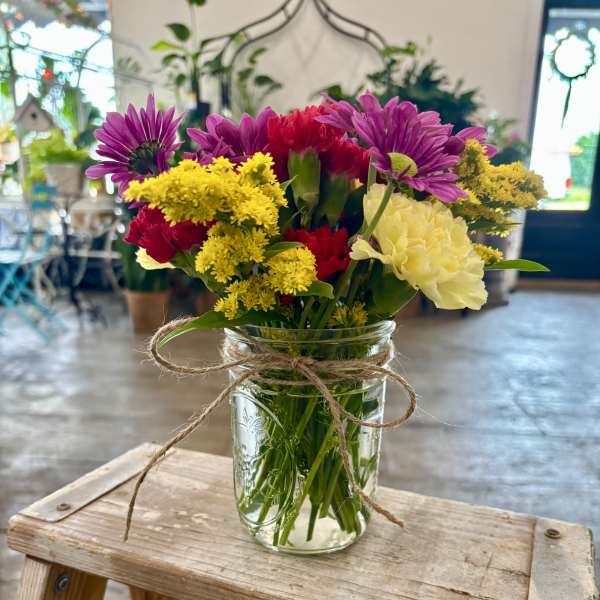 Mixed bouquet of purple, red, yellow, and white flowers in a glass jar vase
