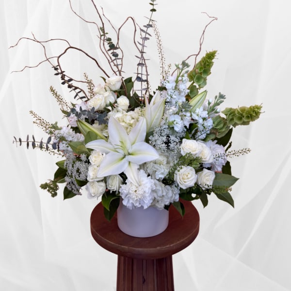 White floral arrangement with lilies and roses in a pale vase