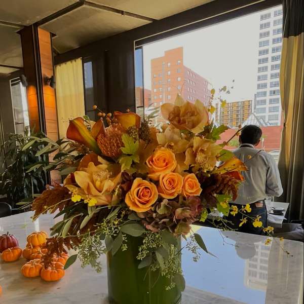 Orange roses and orchids in a green vase on a table