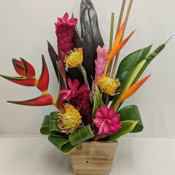 Tropical flower arrangement in a wooden container with pink, orange, and yellow blooms