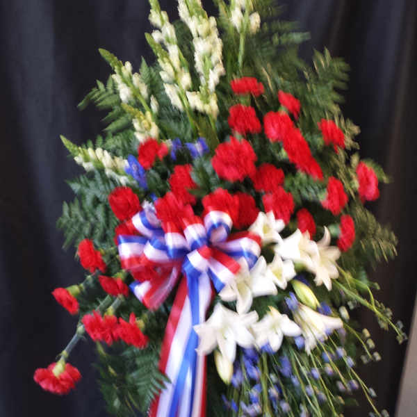 Standing floral spray with red carnations, white lilies, and a red-white-blue ribbon