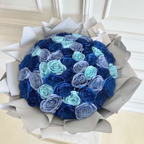 Round bouquet of blue and lavender roses wrapped in pale paper