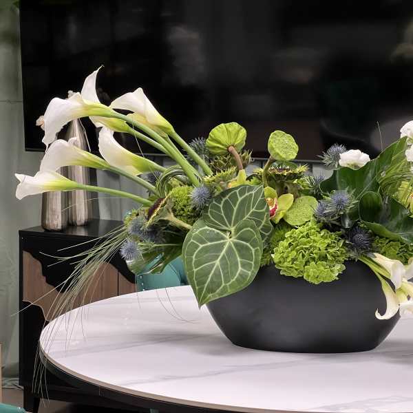 Low floral arrangement with white calla lilies and green blooms in a black bowl