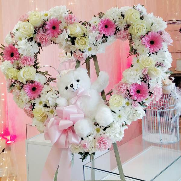 Heart-shaped floral wreath with a teddy bear and pink ribbon
