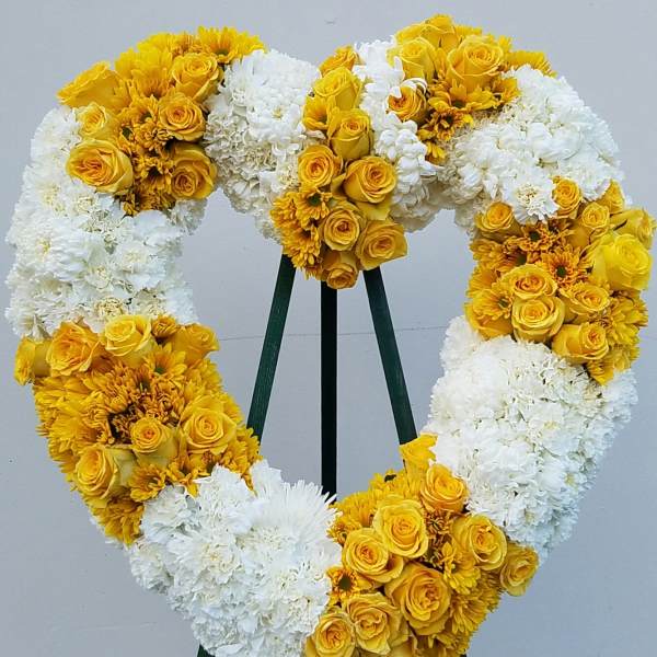 Heart-shaped floral wreath with yellow roses and white blooms on a stand