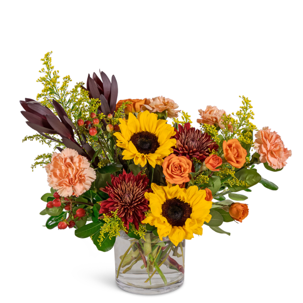 Mixed bouquet of sunflowers, roses, and carnations in a clear glass vase