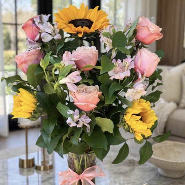 Pink roses and yellow sunflowers in a glass vase with a pink ribbon