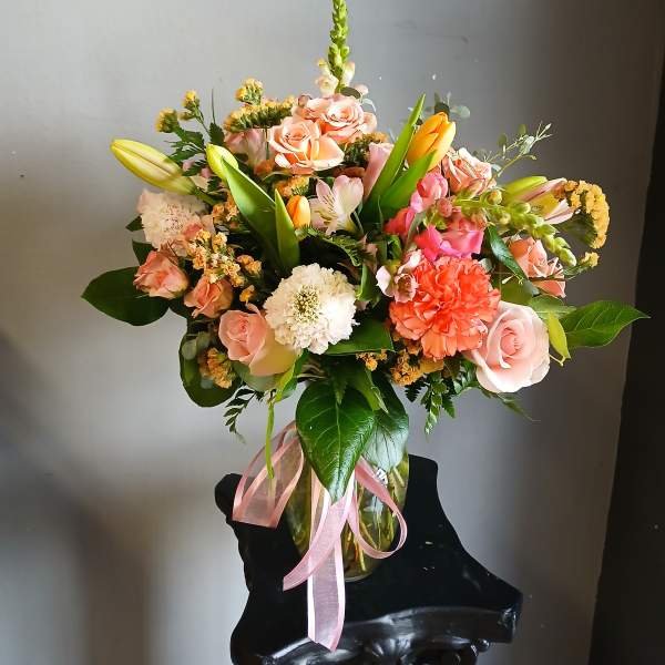 Mixed bouquet of pink roses, lilies, and carnations in a glass vase with a pink ribbon
