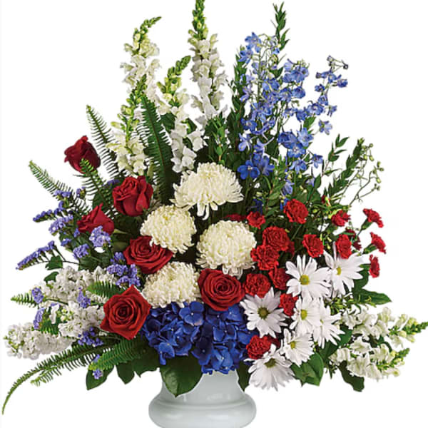 Mixed red, white, and blue floral arrangement in a white pedestal vase