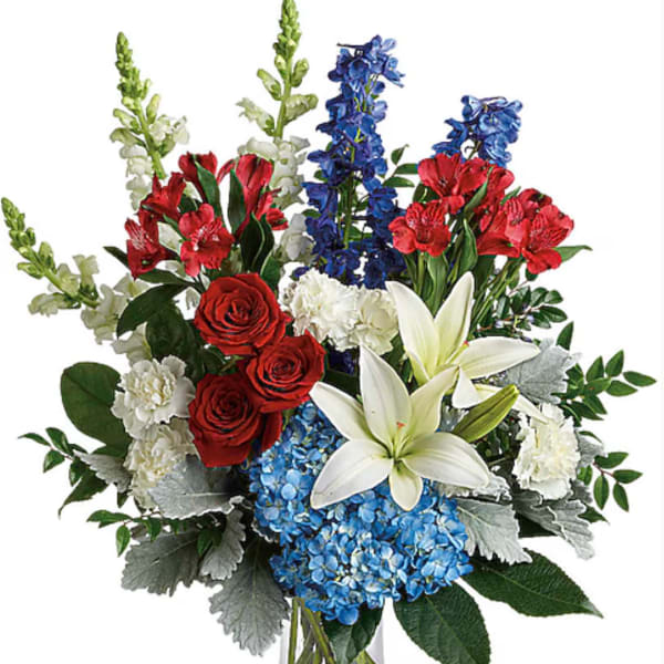Mixed bouquet of red roses, white lilies, blue hydrangeas, and red blooms in a glass vase