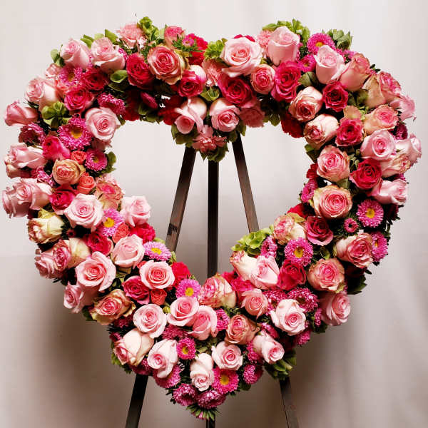 Heart-shaped floral wreath of pink roses and magenta blooms on a stand