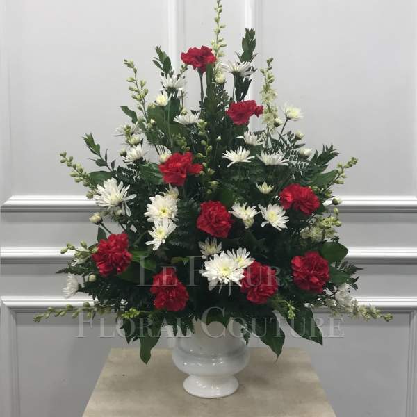 Red carnations and white daisies arranged in a white vase
