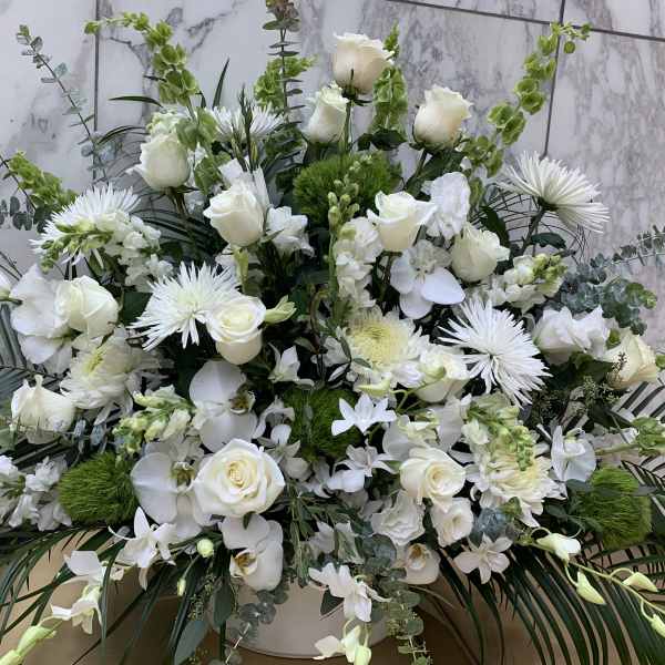 Large white floral arrangement with roses and orchids in a white container