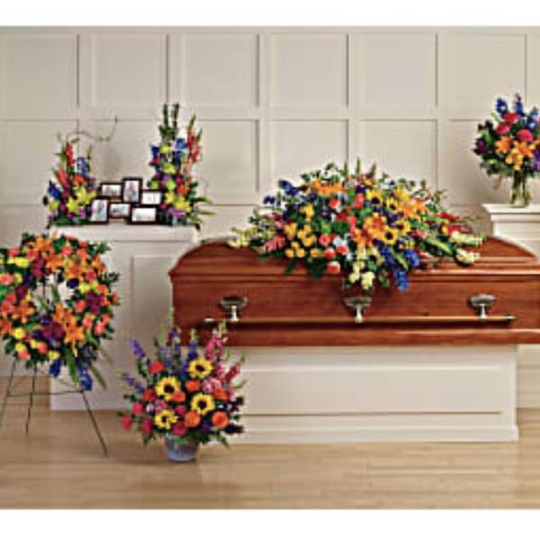 Colorful funeral casket spray with standing floral tributes around a wooden casket