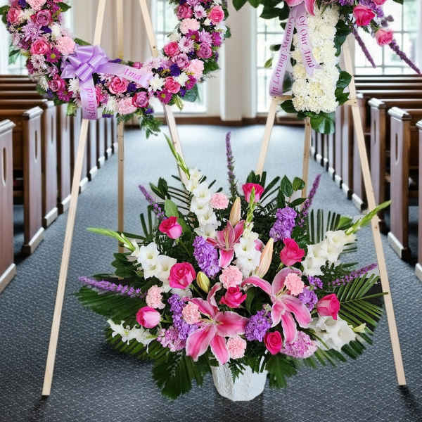 Three pink and white floral funeral tributes on easels in a church aisle
