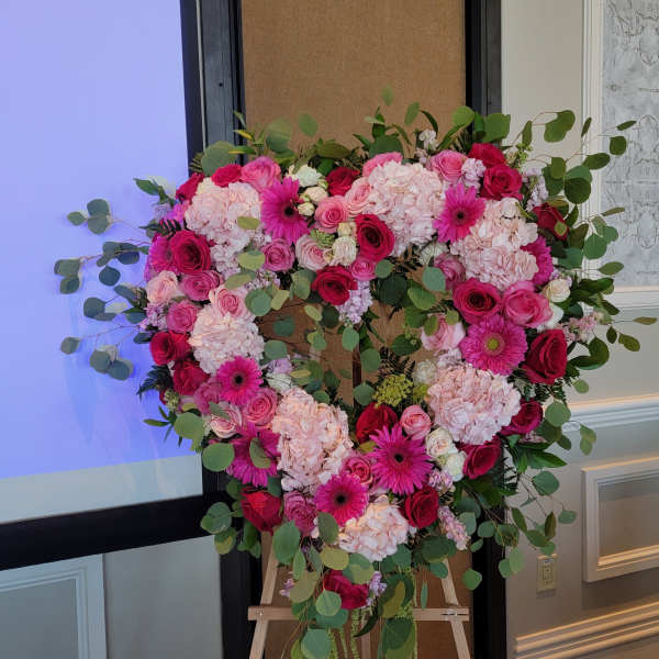 Heart-shaped floral arrangement with pink roses, hydrangeas, and gerbera daisies on an easel