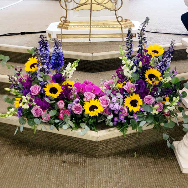 Two floral sprays with sunflowers, pink roses, and purple blooms on a church step