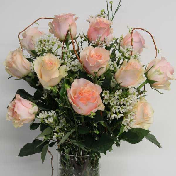 Tall glass vase of pale peach roses with small white accent flowers