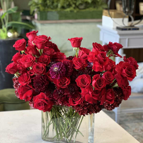 Red roses and dark purple blooms arranged in a clear rectangular vase