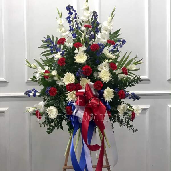 Tall standing floral spray with red, white, and blue flowers on an easel.