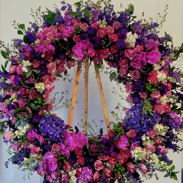 Large floral wreath with pink, purple, and white blooms on a wooden stand