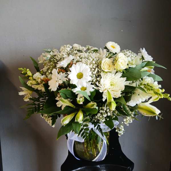 White floral bouquet in a glass vase with a white ribbon